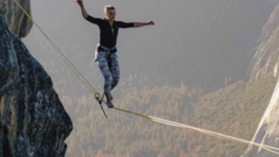 Una persona in bilico su un filo sospeso in cima ad una montagna